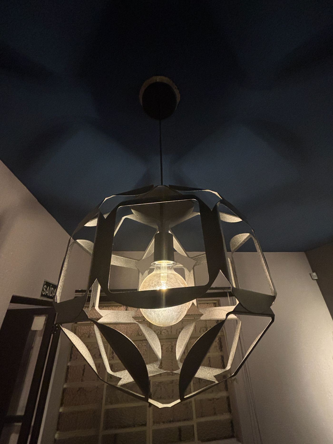 Pendente geométrico preto aceso contra o teto azul-profundo